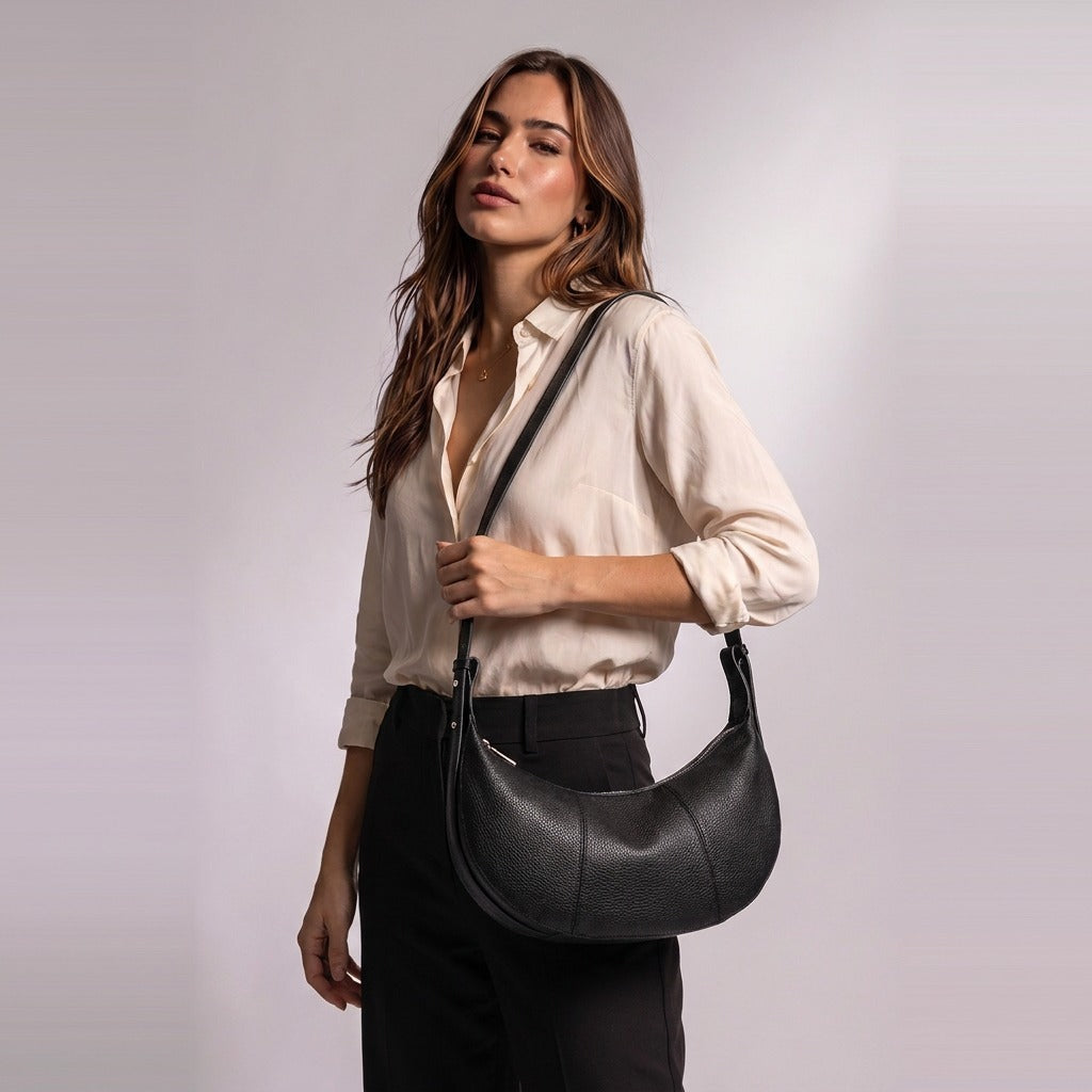 Femme portant le sac demi-lune en cuir Eugénie noir à l'épaule, à hauteur de hanche