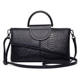 Sac à main en cuir noir Ombeline effet croco, rabat asymétrique et anse ronde, vue de face sur fond blanc