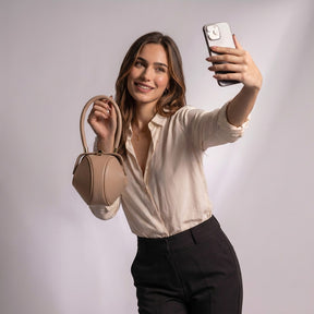 Femme prenant un selfie avec le sac boule Faustine beige à la main