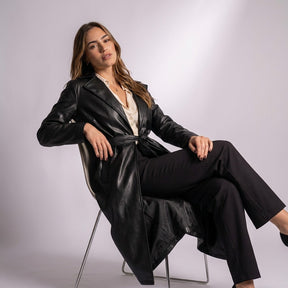 Femme assise sur une chaise portant le trench long Cassandre noir