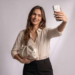 Femme prenant un selfie avec la pochette Honorine blanc cassé sous le bras