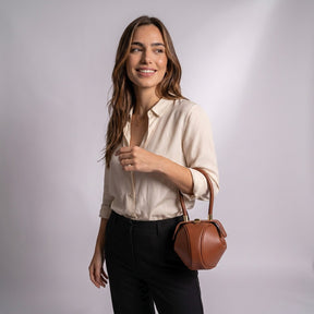 Femme souriante portant le sac boule Faustine cognac au creux du bras