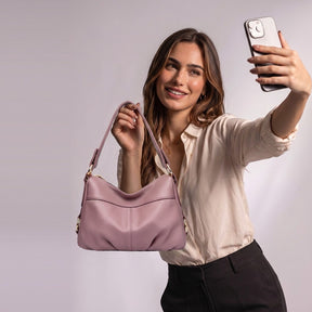 Femme souriante levant le sac à main Joséphine vieux rose tenu par l'anse